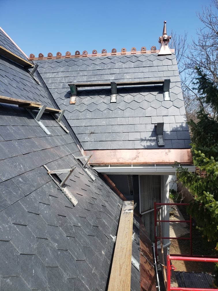 Dark slate roof with copper cresting, finials, and brackets under restoration