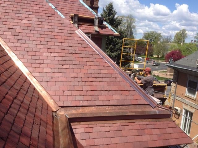 Worker on scaffold installing slate roofing with copper valley flashing